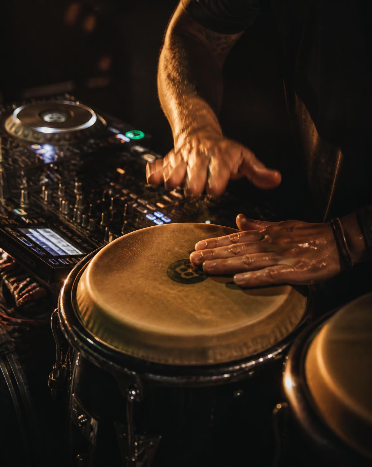 Mani che suonano le congas accanto alla console del DJ